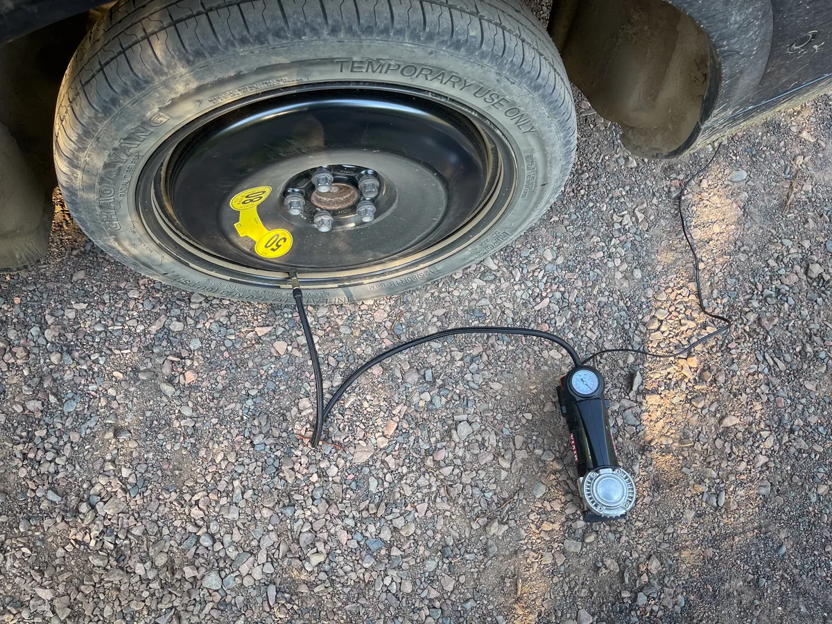 A portable tire inflator being used beside a temporary spare tire.